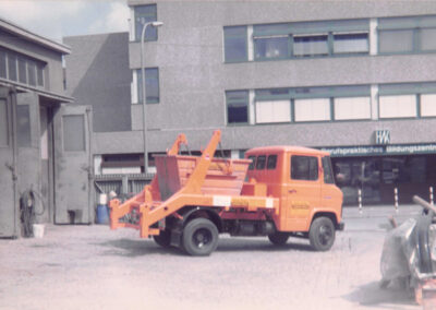 Orangefarbener Absetzkipper-LKW des HAAF Containerdienstes in Seitenansicht auf einem Hof.