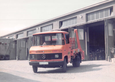Orangefarbener HAAF Containerdienst-LKW vor einer Industriehalle.