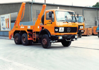 Orangefarbener Mercedes-Absetzkipper-LKW mit Container auf einem befestigten Hof.