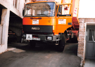 Orangefarbener IVECO-Absetzkipper-LKW des HAAF Containerdienstes in Frontansicht in einer Einfahrt.