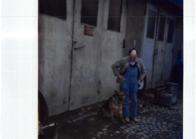 Mitarbeiter mit Hund steht vor einem grauen Werkstatttor auf dem Hof in der Dieselstraße 9 in Würzburg.