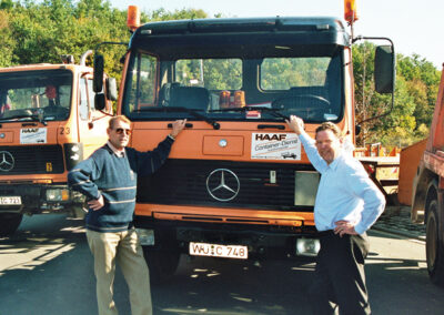 Zwei Firmengründer stehen vor einem orangefarbenen HAAF Containerdienst-LKW.