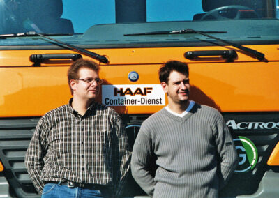 Markus Haaf und Alexander Haaf stehen lächelnd vor einem orangefarbenen HAAF Containerdienst-LKW.