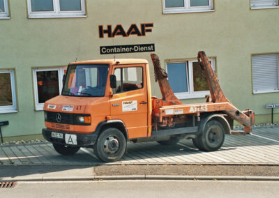 Kleiner orangefarbener Absetzkipper-LKW steht vor dem HAAF Firmengebäude.