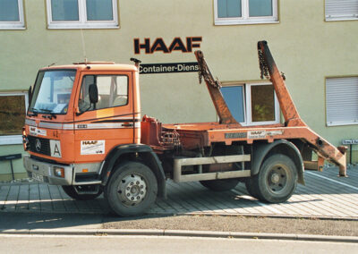 Orangefarbener Absetzkipper-LKW vor der Fassade des HAAF Containerdienstes.