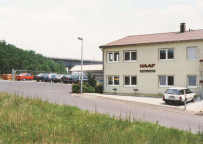 Zweistöckiges Firmengebäude des HAAF Containerdienstes mit Parkplatz an einer Straße.