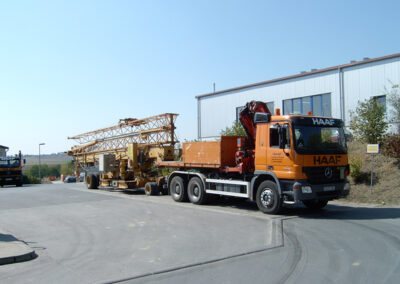 Orangefarbener HAAF-Sattelzug mit Ladekran und Containeranhänger auf einem Betriebshof.