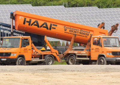 Orangefarbener HAAF-LKW mit großem Aufbau steht vor einer Solaranlage bzw. technischen Anlage im Hintergrund.