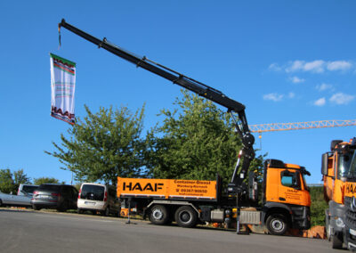 Großer HAAF-Kran-LKW mit weit ausgefahrenem Auslegerarm steht auf einer Straße, im Hintergrund Bäume und Gebäude.