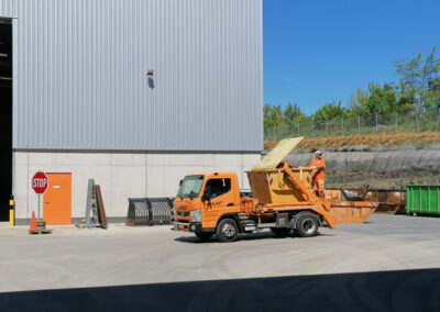 Orangefarbener HAAF-LKW mit Container steht vor der neuen Hallenfassade auf dem Betriebshof.