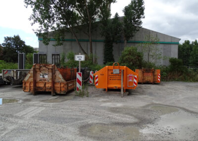 Gruppe orangefarbener HAAF-Container steht auf einem Hof, dahinter hohe Bäume und Grünfläche.