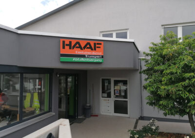 Eingangsbereich eines Bürogebäudes mit HAAF-Schild „Containerdienst Transport Entsorgung“ und Begrünung.