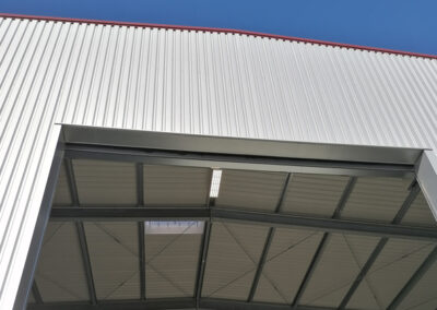 Außendetail des Hallendachs mit roter Attika und heller Blechverkleidung.