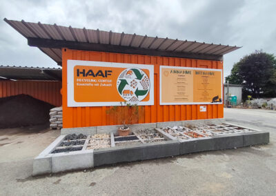 Orangefarbener Info-Container mit HAAF-Aufschrift und RecyclingCenter-Tafel, davor Musterflächen mit verschiedenen Gesteinskörnungen.