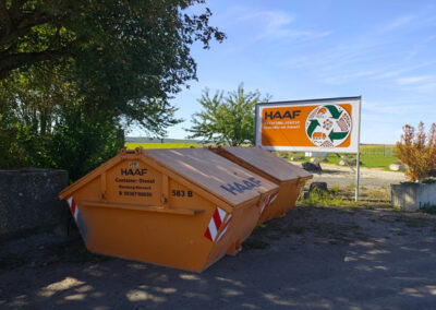 Orangefarbener HAAF-Container steht an der Einfahrt zum RecyclingCenter Bergtheim, daneben ein großes Hinweisschild.