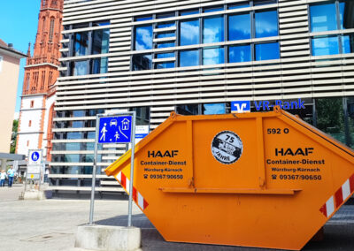 Orangefarbener HAAF-Absetzcontainer steht vor einem modernen Büro- und Glasgebäude in der Stadt.